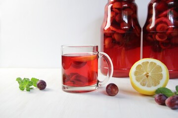 Glass of homemade compote of plums, lemon, mint on white background