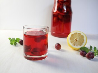 Glass of homemade compote of plums, lemon, mint on white background