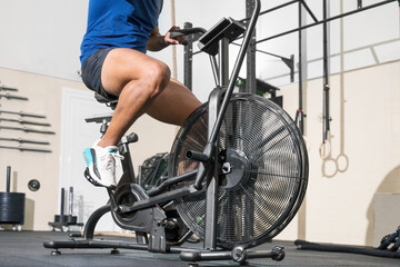 Close up of an unrecognizable man doing cardio training on stationary air bike machine with fan at...