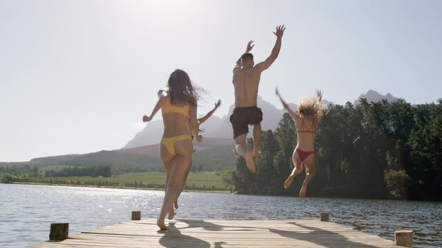 group of friends jumping in lake splashing in water having fun enjoying summer vacation