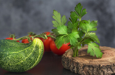 a branch of red tomato and green cucumber with green parsley on a wooden board