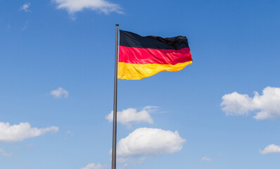 National Flag of Germany fluttering on a pole, against blue sky.