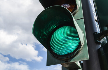 Green traffic light against cloudy blue sky.
