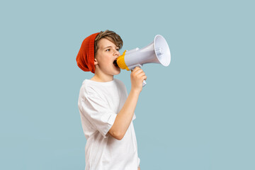 Cute Caucasian teen School boy using megaphone. Red beany hat and white t-shirt on blue banner....