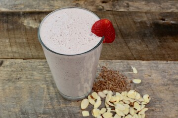 Frothy strawberry protein smoothie shake with flax seed, almonds ingredients shown on a wooden farm house table closeup.