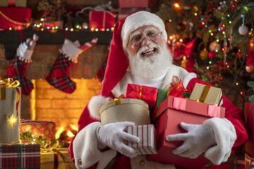 Santa Claus with gift box presents near fireplace and Christmas tree. Wooden house, New Year's...