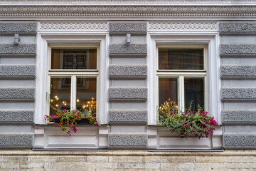 Fototapeta na wymiar Symmetrical windows with plants and flowers on a classic-looking facade.