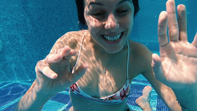 Happy teen girl goes underwater smiling and making funny faces, grimaces