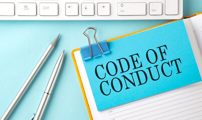 CODE OF CONDUCT text on sticker on the blue background with pen and keyboard