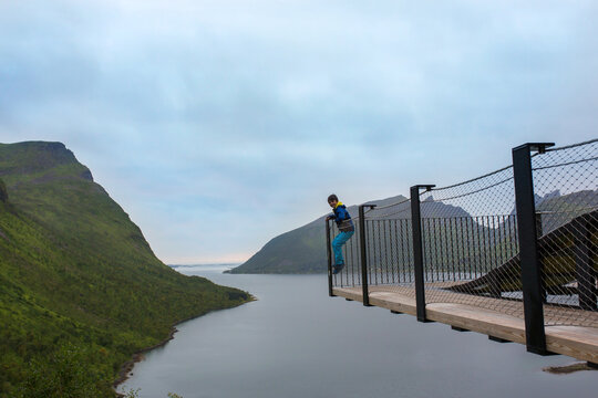 Child, standing on the edge of a 44 meter long viewing platform, overlooking the water of Bergsfjord, enjoying the view on Senja island, Norway