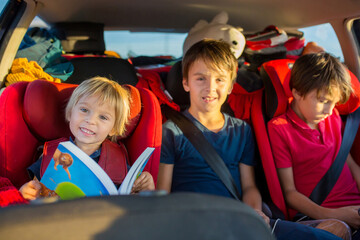 Children, traveling to vacation with car, sitting in carseats and reading books and playing on...