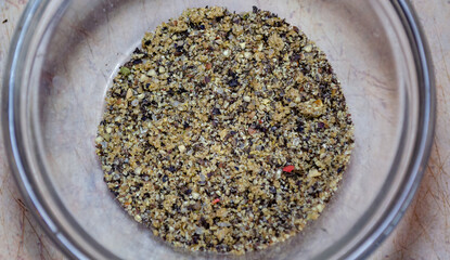 Black ground pepper in a glass bowl on a light pink table