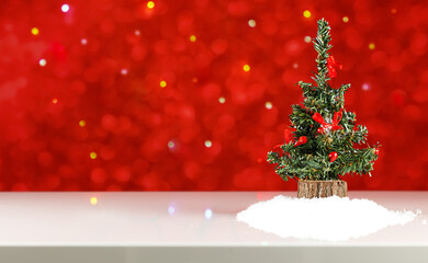 Fototapeta na wymiar toy christmas tree with red decor on a white table against a background of red and multicolored defocused lights