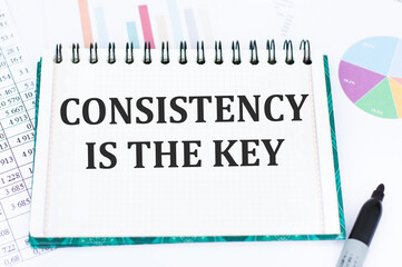 CONSISTENCY IS KEY text on a notebook against the background of financial charts