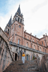 Woman using her mobile phone in front of the Covadonga Sanctuary in Asturias. Vertical photo.