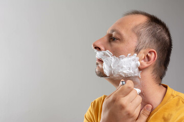 Meddle aged man shaving with foam and razor over gray background.