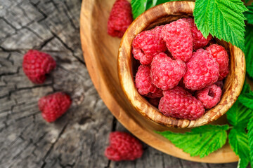 Fresh juicy raspberries in wooden bowl. Summer still life with raspberries on an old wooden table. Copy space .Jar of raspberry jam and fresh berries on wooden background