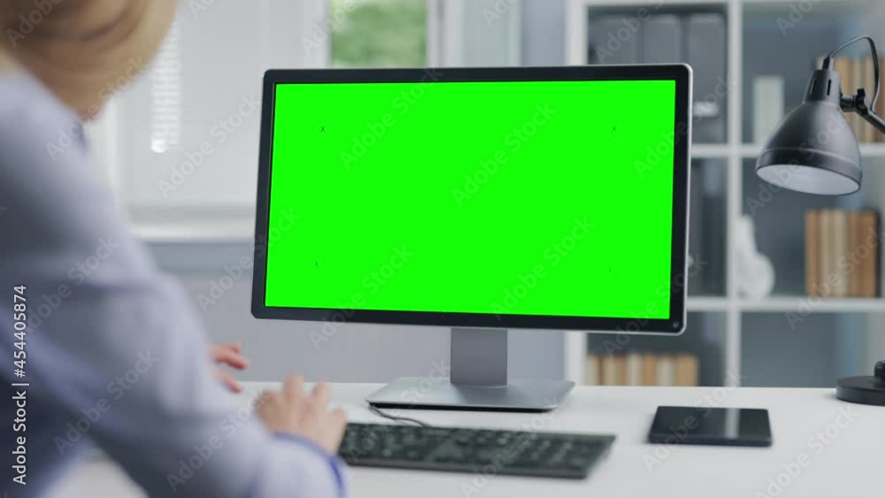 Poster back view of mature lady in formal clothes working on computer with chroma key screen while sitting 