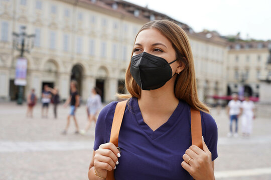 Beautiful university student girl wearing a protective KN95 FFP2 black mask walking in city street