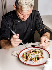 A stylish chef in a black jacket prepares tasty salad with ripe figs, goat Chevre cheese, fresh cucumber roll, beetroot and mustard leaves with tomato sauce. Restaurant dish. Delicious food