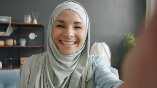 POV portrait of attractive muslim woman speaking and gesturing having online video call looking at camera indoors at home. People and communication concept.