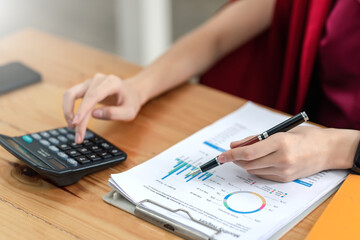 Businesswoman working about calculating budget income stats using calculator  holding a pen pointing at the graph at the office.