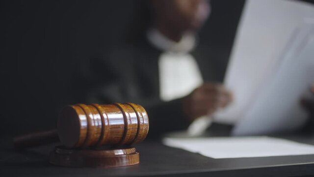 Female judge working with papers in court room, gavel on table, justice symbol