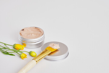 small beautiful flowers, makeup brush and cosmetic red clay in an aluminum jar, natural cosmetics