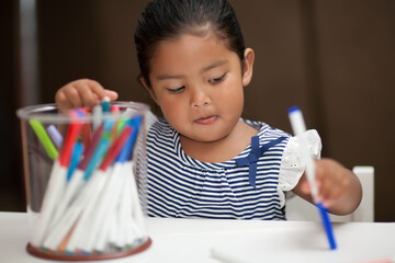 Toddler learning to color and draw with markers on white table