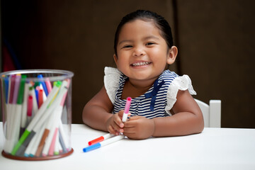 Hispanic young girl on activity table with colorful markers - Powered by Adobe