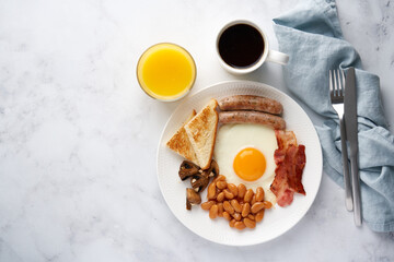 Horizontal top view of classic rustic delicious irish cuisine meal. Fried eggs, grilled sausages, roasted mushrooms, toast, kidney beans, hot coffee and fresh orange juice. Light background copy space