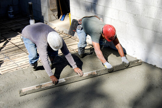 Masons using a screed to level freshly poured concrete