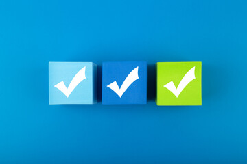 Creative flat lay with three checkmarks close up on blue and green toy cubes in the middle of blue background. Concept of questionary, checklist, to do list, planning or business plans © Irina Ivanova