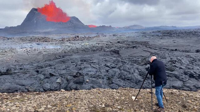 A man films a volcanic eruption from up close with a camera and tripod in Fagradalsfjall eruption Iceland.