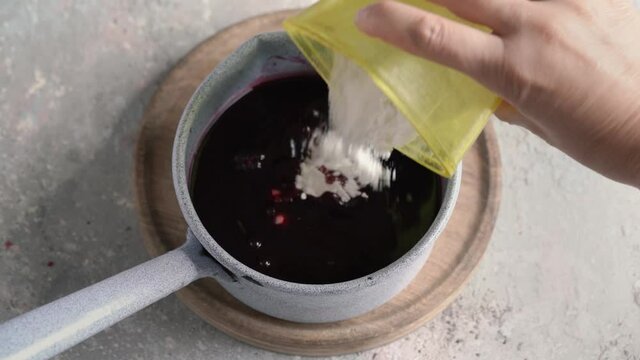 Preparation of homemade black elder syrup - putting sugar into juice from cooked elderberries