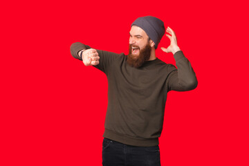 Well surprised bearded man is looking at his wrist watch over red background.