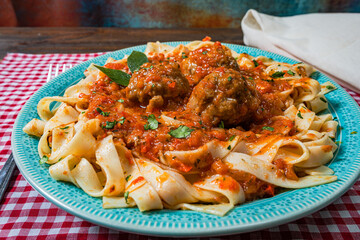 Pasta or Fettuccine with tomato sauce and meatballs in a rustic plate on a checkered tablecloth.