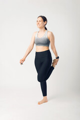 Vertical photo of a smiling young woman is exercising and stretching a little in a white studio.