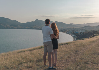 A man and a girl hugging each other, standing on the seashore looking out into the distance
