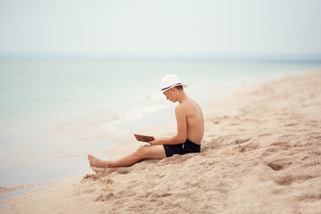 Fototapeta na wymiar A teenager reads a book on the beach