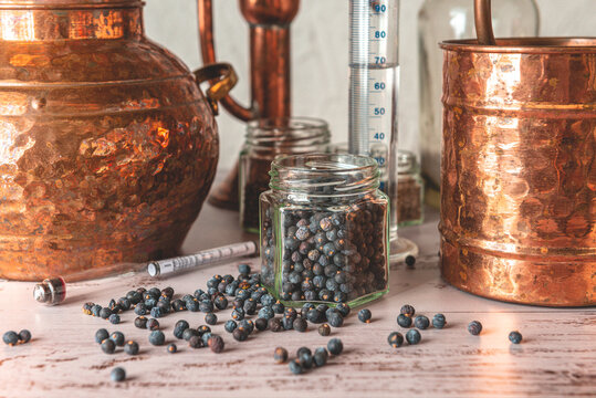 Enebros en primer plano junto a un Alambique de cobre utilizado para destilar con bot&aacute;nicos, enebro, cardamomo y accesorios sobre una mesa de madera.