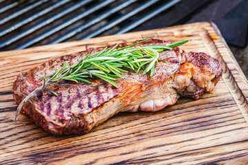 Juicy thick grilled beef steak with rosemary, salt and pepper on wooden cutting board