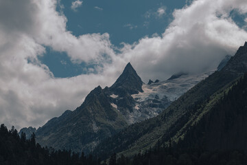 Sharp mountain peak with snow. Landscape of high mountains, river and forest in Dombai