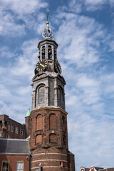 Obraz premium Amsterdam, Netherlands - August 13, 2021: Gray top on red brick Munttoren, clock tower against blue cloudscape, corner of Singel and Muntplein.