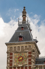 Fototapeta na wymiar Amsterdam, Netherlands - August 14, 2021: Frontal monumental sculpted red stone left tower with wind dial under blue cloudscape.