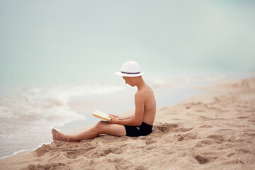 A teenager reads a book on the beach