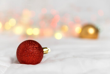 christmas red ball on a white background. In the background, blurry lights from a garland and a golden ball.