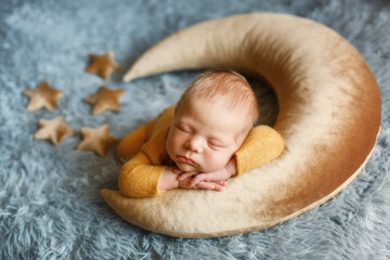 Studio portrait of a newborn cute boy wearing yellow pajama . He is sleeping on a moon shaped...