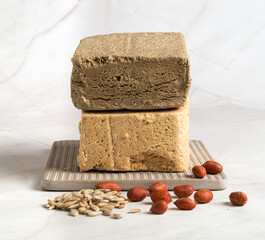 Peanut and sunflower halva lies on a ceramic board next to shelled seeds and nuts-peanuts .Traditional Oriental sweetness for tea drinking.Close-up..