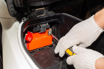 A gloved auto mechanic with a screwdriver unscrews the motorcycle battery terminals for repair or replacement. Car service in a car service.